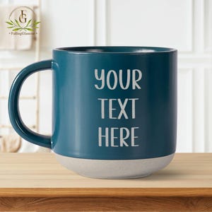 May include: A teal blue ceramic mug with a white base. The mug has the text "YOUR TEXT HERE" printed on the front.