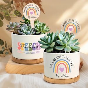 May include: Two white ceramic succulent pots with wooden bases. The left pot has the text "Speech Therapy" with a rainbow design. The right pot has the text "Teaching Kids to Talk Back" with a rainbow design and the name "Ms. Allisa".