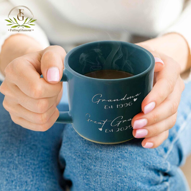 May include: A blue ceramic mug with a white handle. The mug has the text "Grandma Est 1996" and "Great Grandma Est 2025" on it.