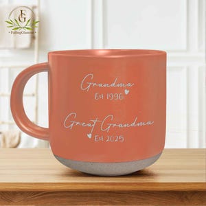 May include: A coral orange ceramic mug with a white handle. The mug has the text "Grandma Est 1996" and "Great Grandma Est 2025" on the front.