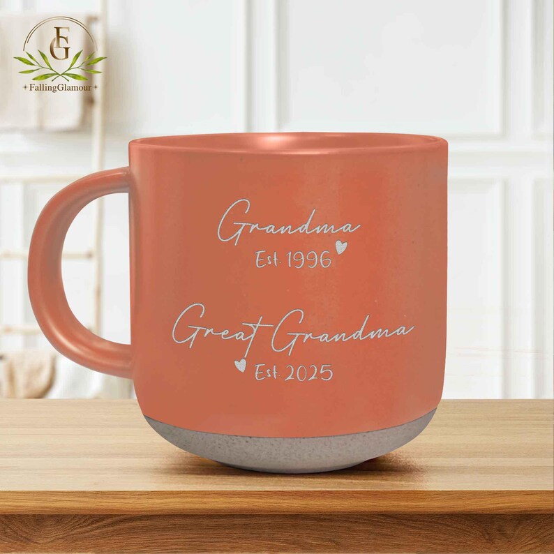 May include: A coral orange ceramic mug with a white handle. The mug has the text "Grandma Est 1996" and "Great Grandma Est 2025" on the front.