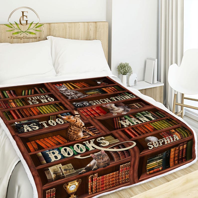 May include: A brown and white fleece blanket with a bookshelf design. The bookshelf is filled with books and has a cat on each shelf. The text on the blanket reads "There is no such thing as too many books".