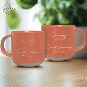 May include: Two orange ceramic mugs with white text. The mug on the left says "Grandma Est 1996 Great Grandma Est 2025". The mug on the right says "Grandpa Est 1996 Great Grandpa Est 2025".