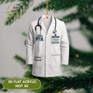 May include: White Physician Assistant coat ornament with a stethoscope, the letters "PA", and the name "James Dyson". The ornament also has the text "Physician Assistant" and "Dec 14th, 2025". The bottom of the ornament reads "2D FLAT ACRYLIC NOT 3D".
