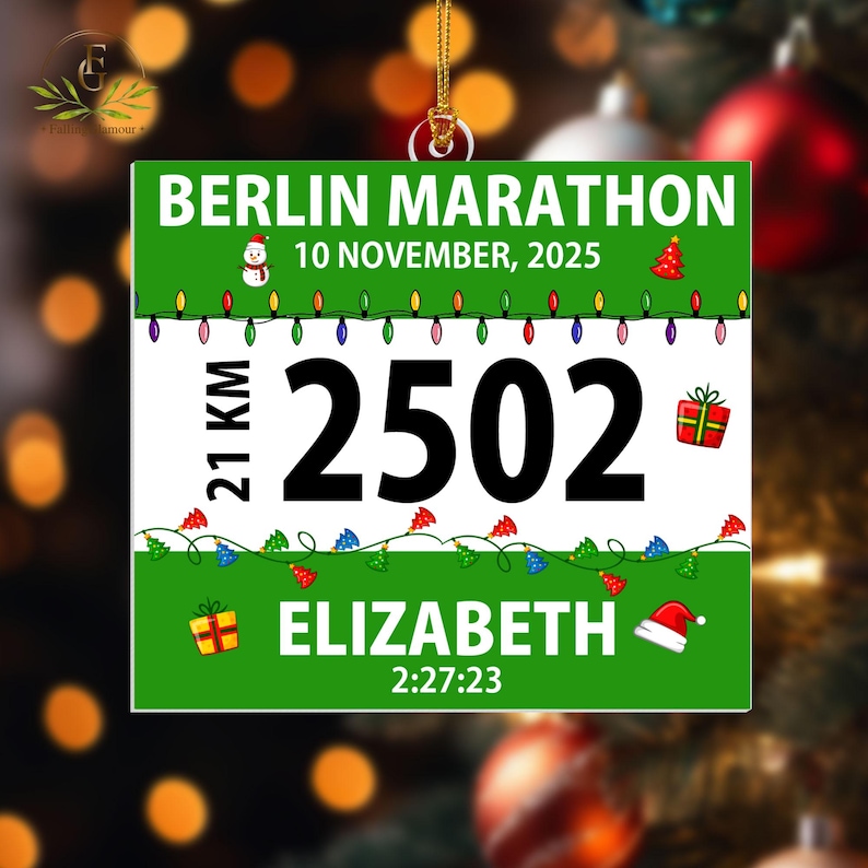 May include: A square Christmas ornament featuring a Berlin Marathon race bib design. The green and white graphic displays the text BERLIN MARATHON, 10 NOVEMBER, 2025, 21 KM, 2502, ELIZABETH, and 2:27:23, decorated with a snowman, Christmas trees, lights, and gifts.