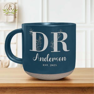 May include: A blue ceramic mug with a white design. The mug has the letters "DR" with floral accents and the text "Anderson EST. 2025".