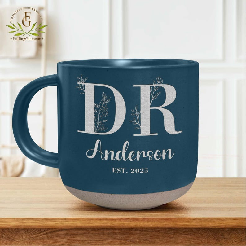 May include: A blue ceramic mug with a white design. The mug has the letters "DR" with floral accents and the text "Anderson EST. 2025".