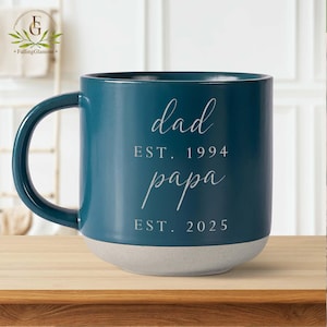 May include: Teal blue ceramic mug with a white base. The mug has the text "dad est. 1994 papa est. 2025" written on it.
