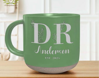 May include: Green ceramic mug with a white inscription that reads "DR Anderson EST. 2025". The mug has a white floral design around the letters.