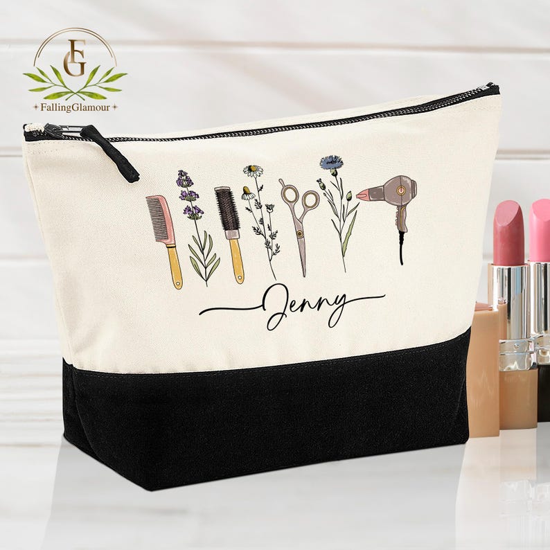 May include: A canvas makeup bag with a black base and a cream-colored top. The bag features a black zipper and a design of salon tools and flowers. The name "Jenny" is written in cursive below the design.