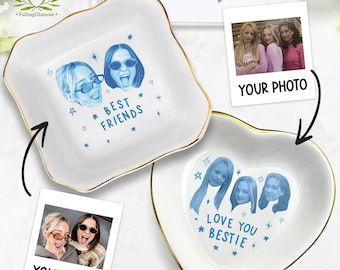 May include: Two white ceramic trinket dishes with gold rims. One is square with "BEST FRIENDS" and two blue portraits. The other is heart-shaped with "LOVE YOU BESTIE" and four blue portraits. Includes two photos with the text "YOUR PHOTO".