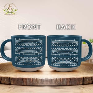 May include: A pair of ceramic mugs with a dark teal exterior and a light gray base. The front and back of each mug feature a white geometric pattern. The word "FRONT" and "BACK" are printed above the mugs.