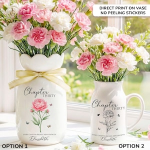 May include: Two white ceramic vases with floral arrangements. One vase has a scalloped top and a yellow ribbon, the other is a mug. Both have a floral design, the text "Chapter Thirty", and the name "Elizabeth".