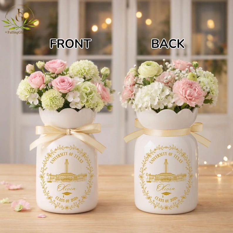 Pu&ograve; includere: Due vasi in ceramica bianca, ciascuno con una composizione floreale di fiori rosa e bianchi. I vasi hanno un nastro dorato e un emblema dorato con la scritta "University of Texas", un nome e "Class of 2026".