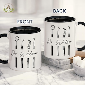 May include: White ceramic mug with a black interior and handle, displaying dental instruments and the name "Dr. Wilson" in black script. A mug designed for dentists and dental professionals.