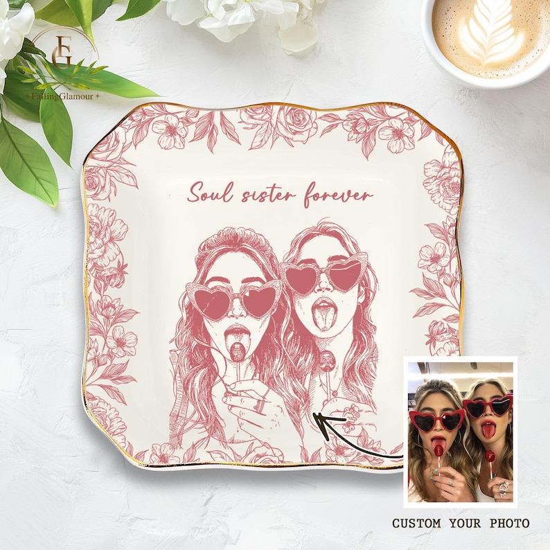 May include: A decorative, off-white ceramic plate with a gold rim and a floral border. The plate features a pink illustration of two women wearing heart-shaped sunglasses and the text "Soul sister forever". A small photo is included.