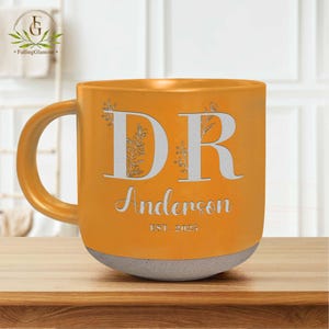 May include: A yellow ceramic mug with a white design. The mug has the letters "DR" with floral accents and the text "Anderson EST. 2025".