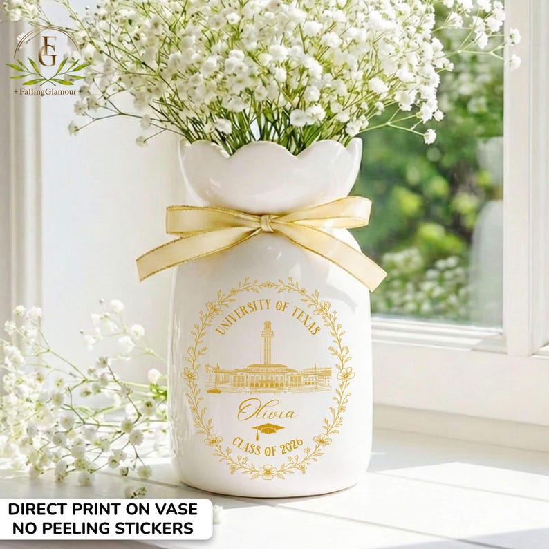 Pu&ograve; includere: Un vaso di ceramica bianca con la parte superiore smerlata, pieno di fiori bianchi e legato con un nastro dorato. Il vaso presenta una stampa dorata del sigillo dell'Universit&agrave; del Texas, il nome "Olivia" e "Classe del 2026".