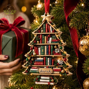 May include: A Christmas tree-shaped wooden ornament featuring multiple shelves filled with miniature books in red, green, and white. The ornament is topped with a gold star, decorated with tiny lights, and includes a nameplate with the name Sarah.