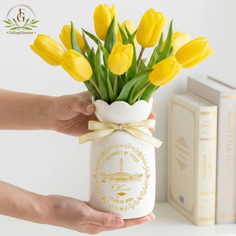 Pu&ograve; includere: Un vaso di ceramica bianco con bordo smerlato, legato con un nastro dorato, contiene un bouquet di tulipani giallo brillante. Il vaso &egrave; decorato con un'illustrazione dorata di un edificio e il testo "UNIVERSITY OF TEXAS", "Olivia" e "CLASS OF 2020".