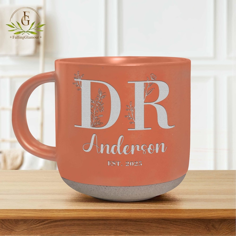May include: A coral orange ceramic mug with a white handle. The mug has the letters "DR" with floral designs and the text "Anderson EST. 2025" in white.