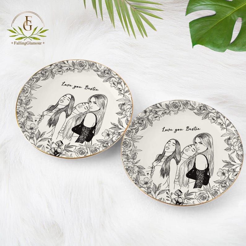 May include: Two white ceramic plates with a gold rim. Each plate features a black and white illustration of three women and the text "Love you Bestie". The plates are surrounded by a floral border.