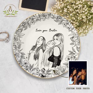 May include: A white ceramic plate with a gold rim, featuring a black and white floral border and a sketch of three women with the text "Love you Bestie." A small photo is included with the text "Custom Your Photo."