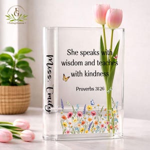 May include: A clear acrylic vase with a floral design and the text "She speaks with wisdom and teaches with kindness" and "Proverbs 31:26". The vase holds pink tulips. The name "Miss. Emily" is printed on the side.