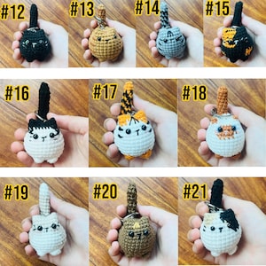 May include: A collection of handmade crochet cat keychains in various colors and patterns. Each keychain features a small, round cat body with a tail and a keyring. The cats are in shades of black, brown, orange, gray, and white.