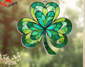 May include: A green stained glass shamrock hanging in a window. The shamrock is made of many small pieces of glass in shades of green and has a silver chain.