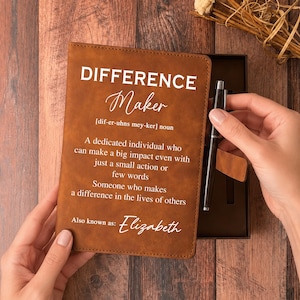 May include: A brown leather journal with the words "DIFFERENCE Maker" and a definition printed on the cover. The journal is open, revealing a black pen and a gift box. The text also includes the name "Elizabeth".