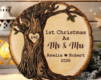 Pode incluir: Um ornamento de fatia de madeira redonda com um design de árvore gravado a laser e um coração contendo as iniciais A R. O texto diz 1st Christmas As Mr & Mrs, Amelia, Robert e 2026. O veio da madeira é visível na superfície clara.