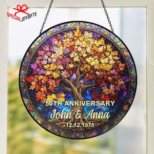 May include: A round stained glass window with a tree design. The tree has colorful leaves in shades of red, orange, yellow, and purple. The text reads "50th Anniversary John & Anna 12.12.1975". The window is hanging by a chain.