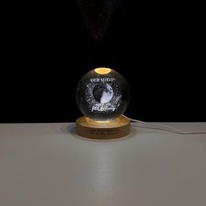 May include: A clear glass sphere night light featuring an etched moon graphic, the text "OUR MOON", "JUNE 22, 2028", and "Phil & Penny". The sphere rests on a circular wooden base engraved with the text "Our First Night as Mr & Mrs Vondras".