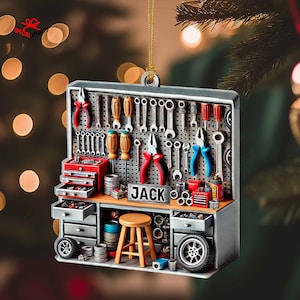 May include: A gray and silver workshop ornament with a pegboard displaying various tools, including wrenches, screwdrivers, and pliers. The name "JACK" is displayed on a small sign. A small wooden stool and a tire are also visible.