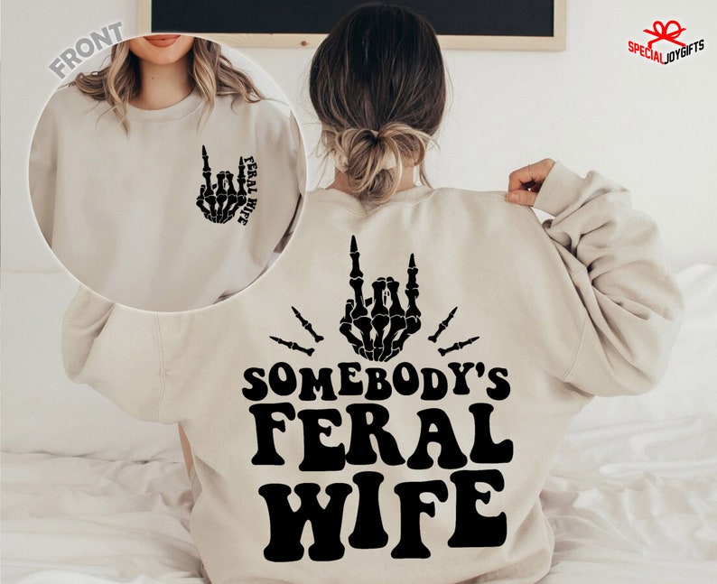 May include: A beige sweatshirt with a black skeleton hand design on the front and the text "Somebody's Feral Wife" on the back.