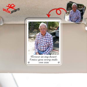 May include: A clear acrylic photo display featuring a color photograph of an older man in a red, white, and blue plaid shirt. The text "Forever in my heart, I miss you every mile. 1948-2026" is printed below the photo. The display is mounted on a car visor.