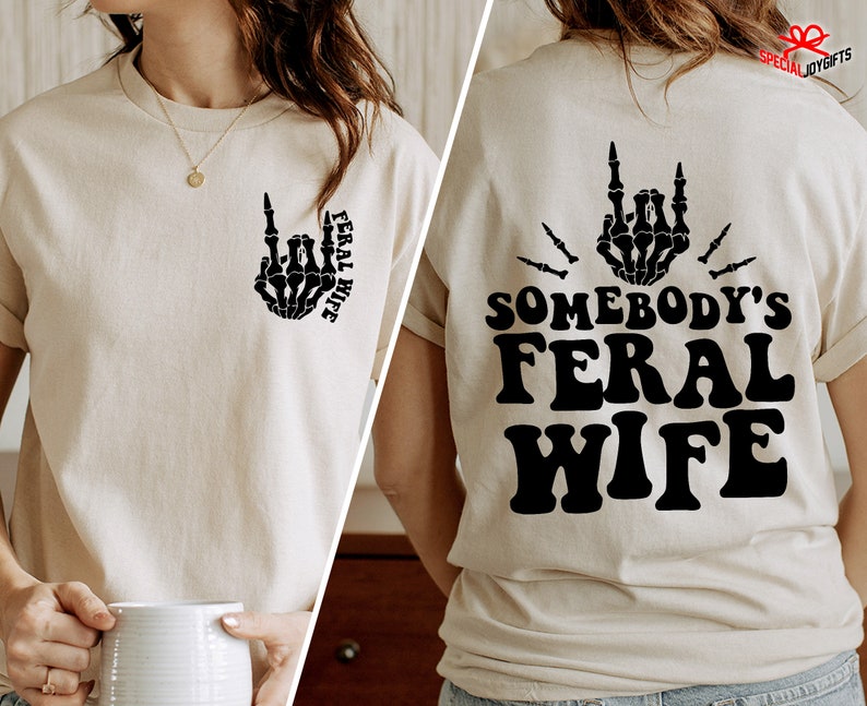 May include: A beige t-shirt with a black skeleton hand making a rock and roll gesture and the text "Feral Wife" on the front. The back of the shirt has the text "Somebody's Feral Wife" in black.