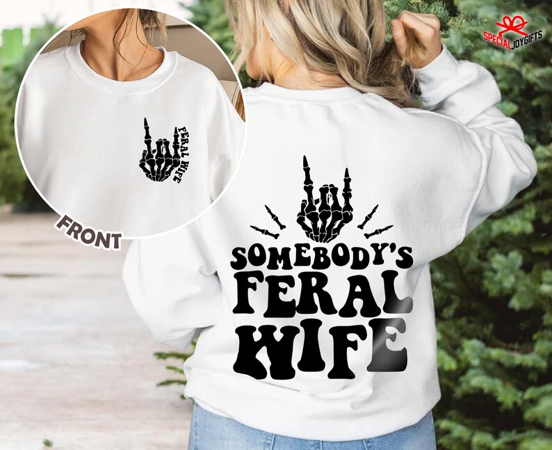 May include: White sweatshirt with a black skeleton hand making a rock and roll sign with the text "Somebody's Feral Wife" on the back. The front of the sweatshirt has a smaller version of the skeleton hand with the text "Feral Wife" on the front.