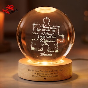 May include: A clear glass sphere lamp on a cylindrical wooden base. The sphere features an etched puzzle piece design with the text: Never forget you are the piece that made the difference, and the name Amanda. The base has engraved text.