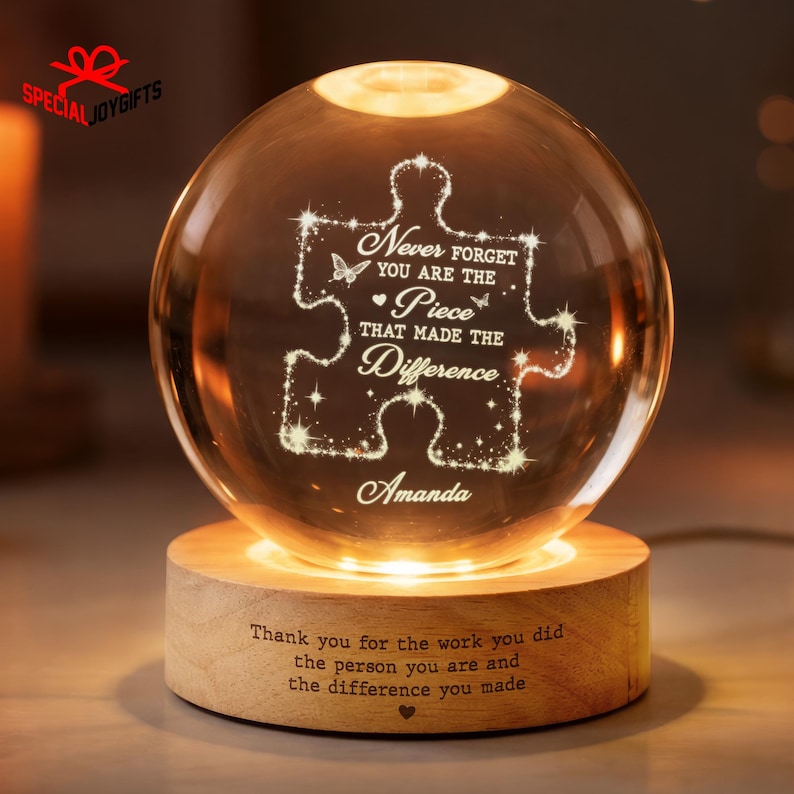 May include: A clear glass sphere lamp on a cylindrical wooden base. The sphere features an etched puzzle piece design with the text: Never forget you are the piece that made the difference, and the name Amanda. The base has engraved text.
