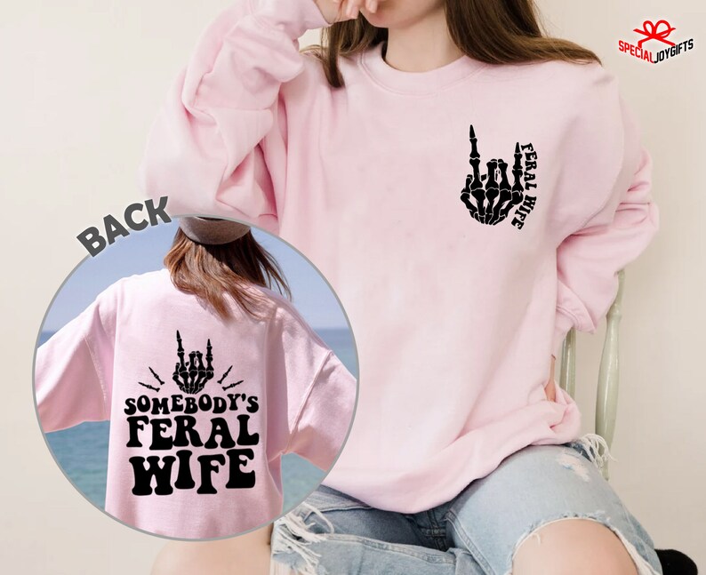 May include: Pink sweatshirt with a black skeleton hand giving the middle finger and the text "Feral Wife" on the front. The back of the sweatshirt has a black skeleton hand giving the middle finger and the text "Somebody's Feral Wife".