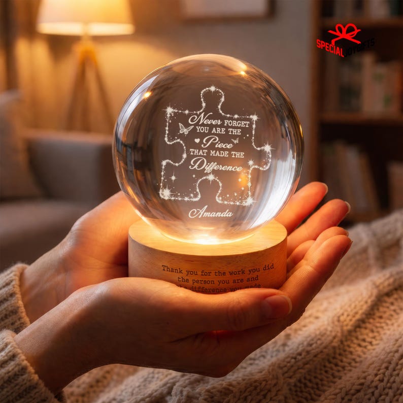 May include: A clear glass sphere resting on a circular wooden base. The sphere features an etched puzzle piece design with the text: Never forget you are the piece that made the difference, and the name Amanda. The base has engraved text.
