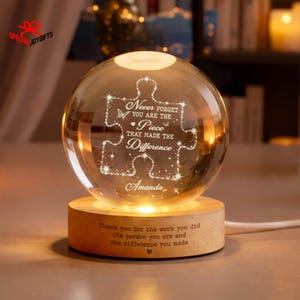 May include: A clear glass sphere night light resting on a round wooden base. The sphere features an etched puzzle piece design with the text: Never forget you are the piece that made the difference, and the name Amanda. The base reads: Thank you for the work you did, the person you are and the difference you made.