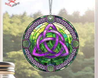May include: A circular stained glass ornament featuring a purple Celtic knot design with green and yellow accents. The ornament is surrounded by a decorative border.