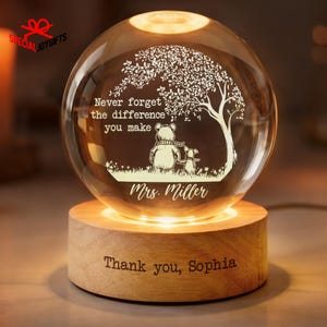 May include: A clear glass sphere with an etched design of a bear and a smaller animal under a tree, with the text "Never forget the difference you make Mrs. Miller." The sphere sits on a wooden base with the text "Thank you, Sophia."