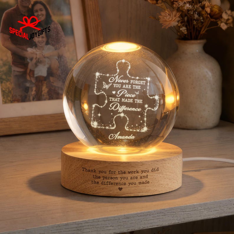 May include: A clear glass sphere lamp resting on a circular wooden base. The sphere features an etched puzzle piece design with the text "Never forget you are the piece that made the difference" and the name "Amanda". The base has engraved text.