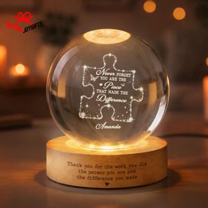 May include: A clear glass sphere lamp resting on a circular wooden base. The sphere features an etched puzzle piece design with the text "Never forget you are the piece that made the difference" and "Amanda". The base has engraved text.