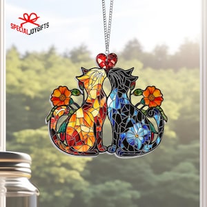 May include: A stained glass window hanging featuring two cats kissing with a red heart above them. The cats are surrounded by flowers and have a mosaic design.