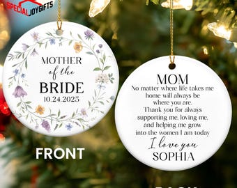 May include: A round, white ceramic Christmas ornament with gold string. The front reads "MOTHER of the BRIDE 10.24.2025" surrounded by a floral wreath. The back says "MOM" and a personalized message.